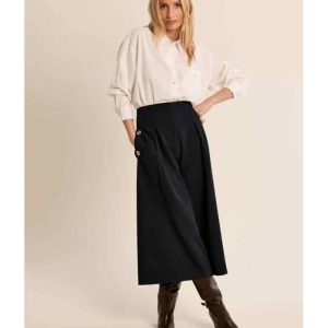 Une jupe culotte au tombé fluide et noir profond, à larges plis sculptés et boutons dorés sur les poches — la pièce tailleur qui réconcilie la liberté de mouvement du pantalon et l'élégance graphique de la jupe longue. Référence : P1849EN