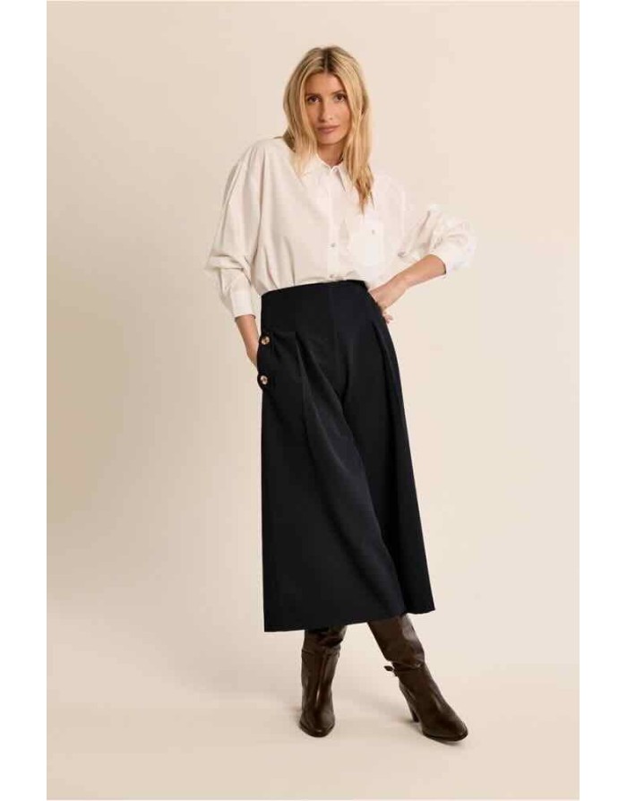 Une jupe culotte au tombé fluide et noir profond, à larges plis sculptés et boutons dorés sur les poches — la pièce tailleur qui réconcilie la liberté de mouvement du pantalon et l'élégance graphique de la jupe longue. Référence : P1849EN